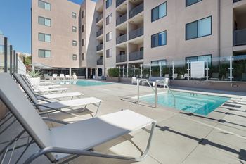 A pool area with sun loungers and a building in the background.